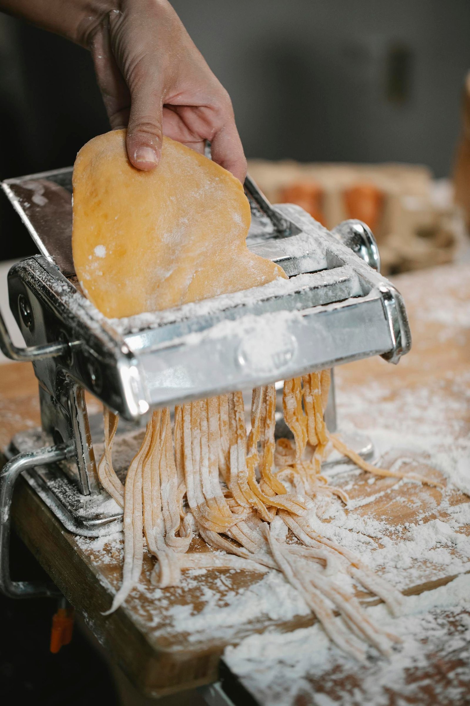 Crop anonymous person making pasta with pasta cutter on wooden table covered with flour