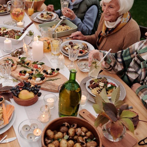 From above crop people enjoying festive dinner with snacks at garden table with candles burning