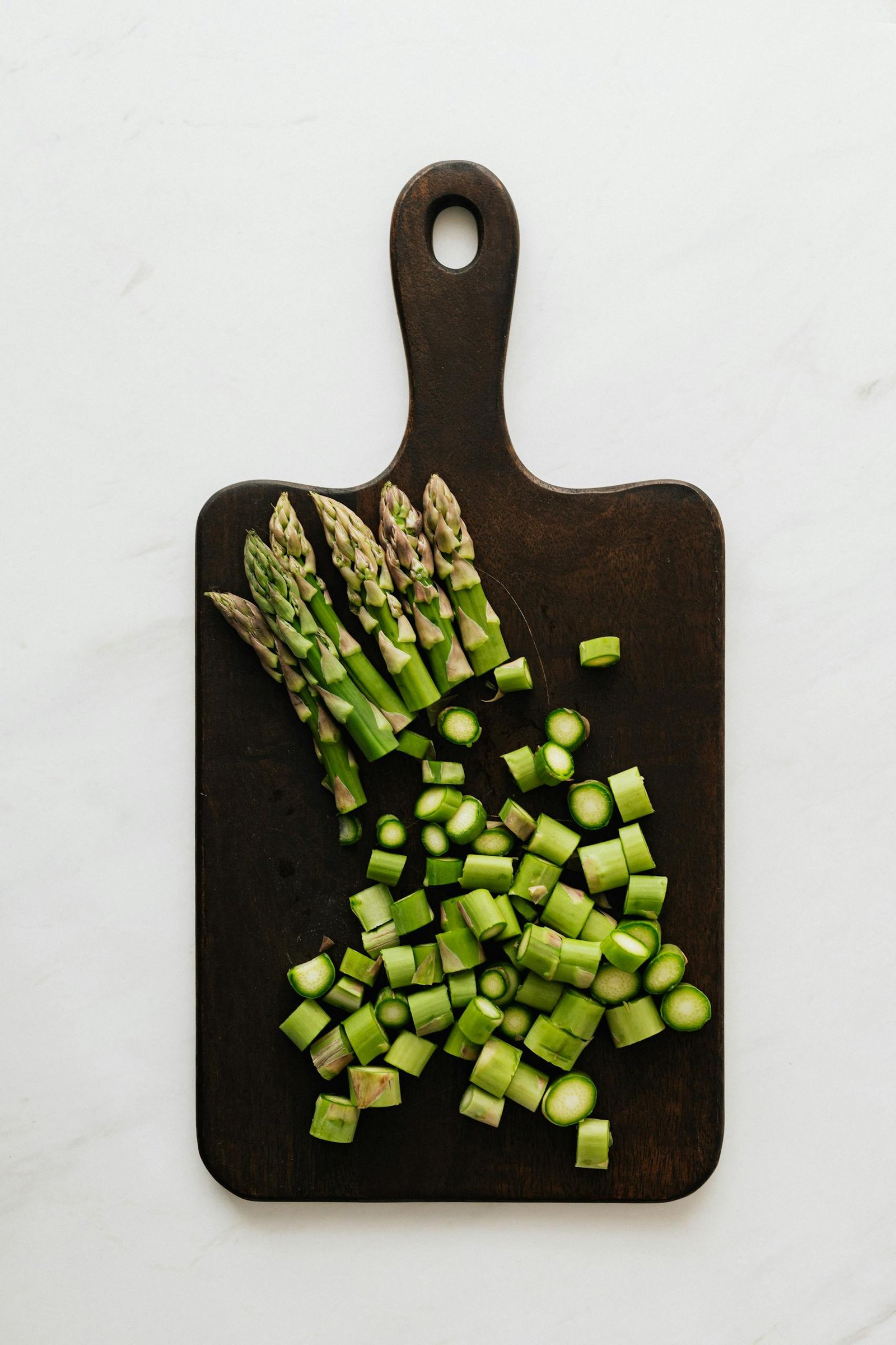 Top view of sliced green stem of asparagus composed on dark cutting board placed on white table