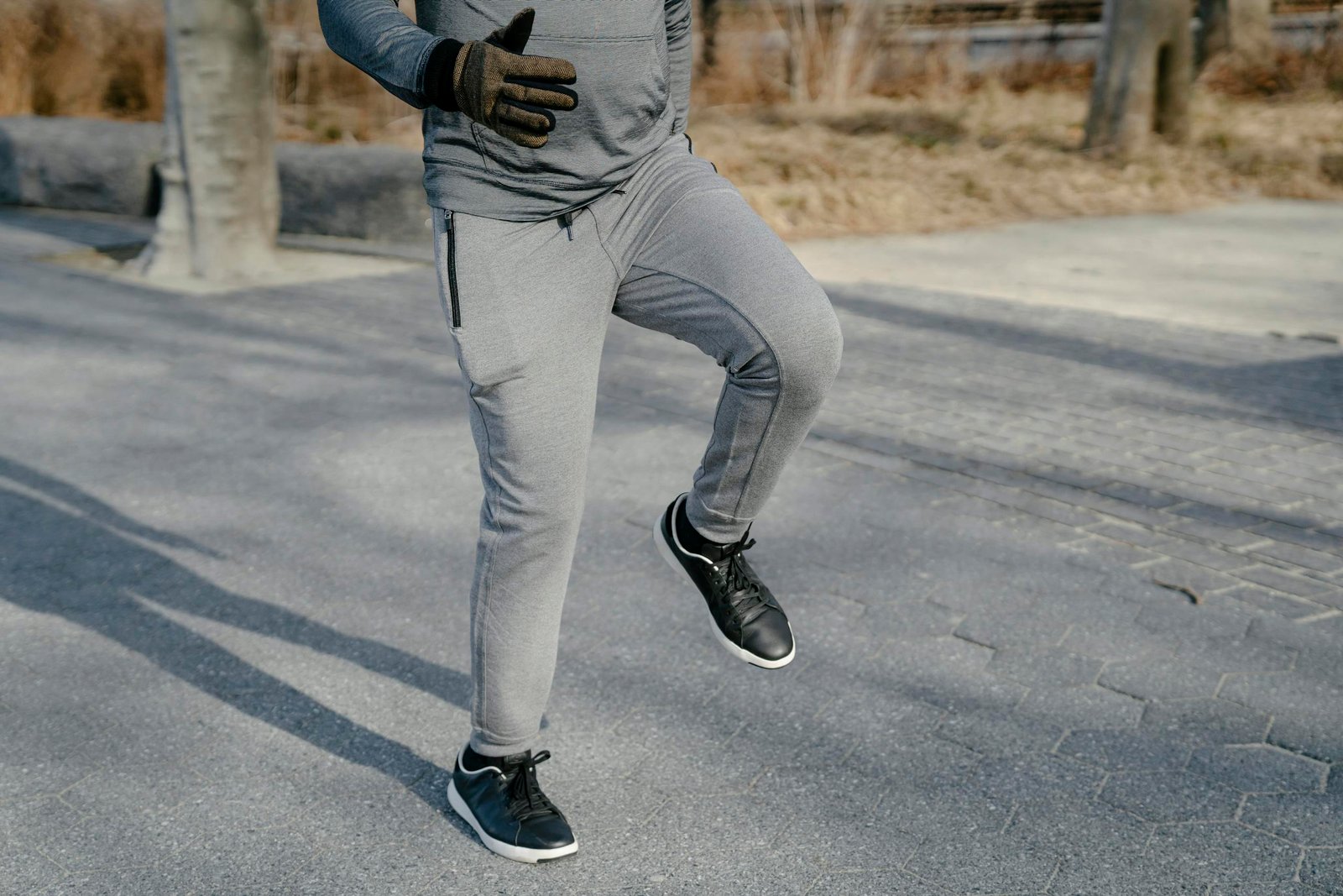 Crop anonymous male in gray sport trousers and black sneakers warming up legs in asphalt road