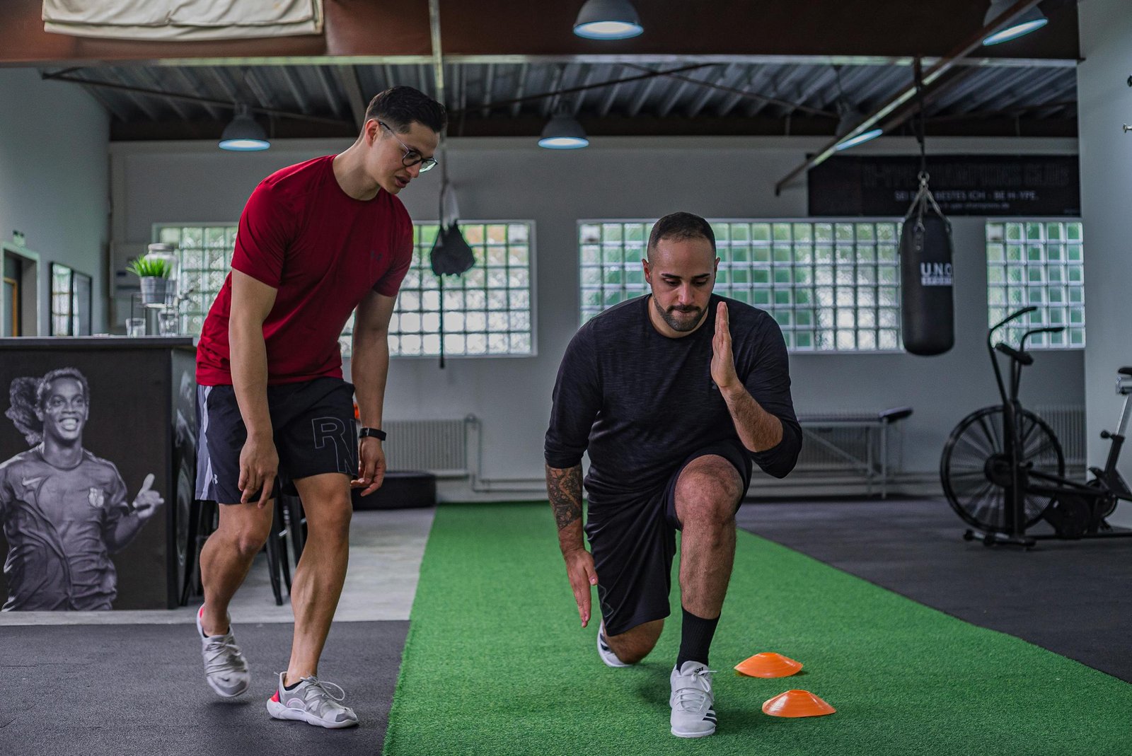 Full body of focused man in sportswear doing stretching exercises with coach in contemporary fitness center